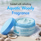 mCaffeine By The Blues Brightening Body Scrub 175 g - aquatic woody fragrance visual with the open tub on sand and shells